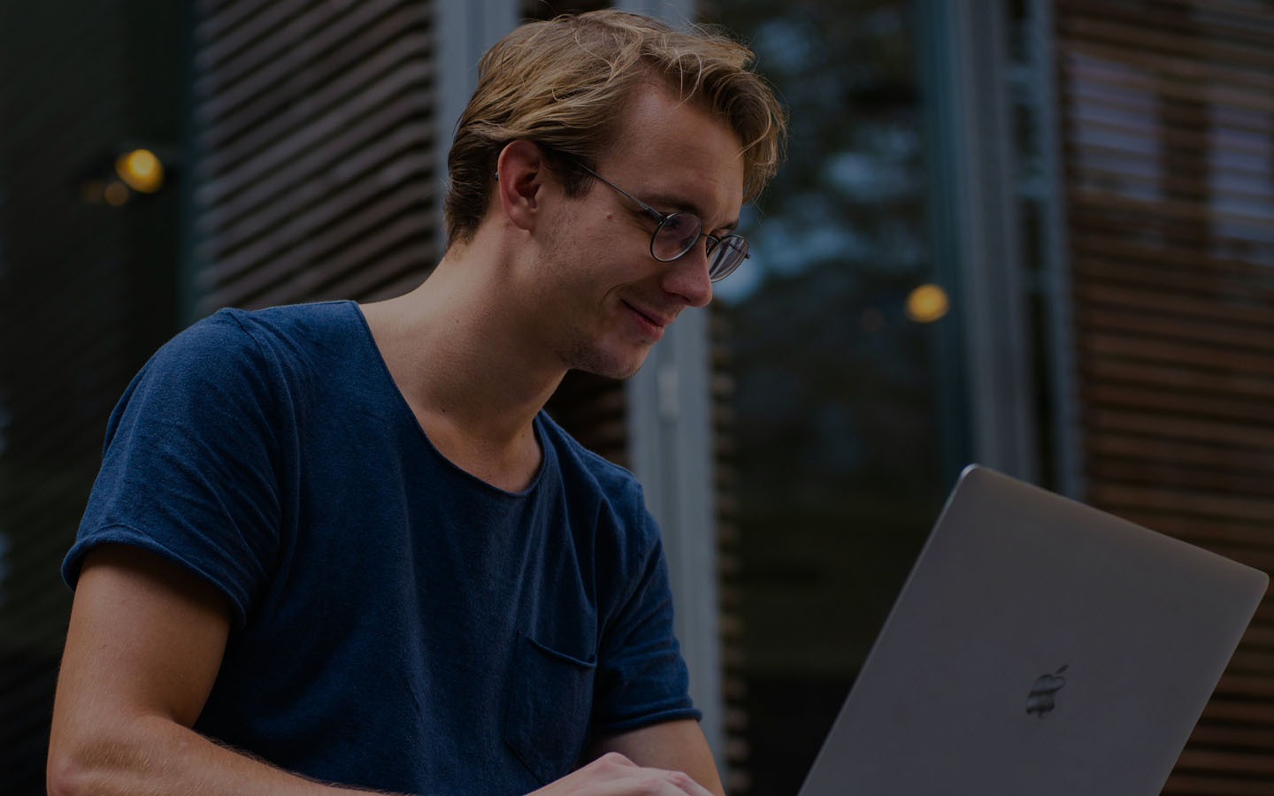 Homem de camisa azul no quintal olhando para o notebook e sorrindo